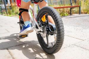 Close up view of legs of little girl rides a two-wheeled bicycle Ii the courtyard of apartment buildings in summer, Europe. High quality photo