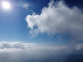 Aerial view. The drone flies over foggy and fluffy clouds. Blue sky sun and sea fog. Abstract aerial nature summer ocean sunset sea and sky background. Vacation, travel and holiday concept photo