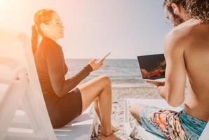 Man woman laptop sea. Working remotely on seashore. Happy successful couple, freelancers working on sea beach, relieves stress from work to restore life balance. Freelance, remote work on vacation photo