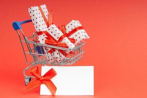 Trolley full of gifts on a red background with mock up and copy space. Concept for christmas, holidays, discounts and shopping. photo