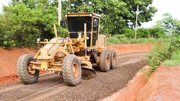 Grader machine leveling gravels on a dirt road in preparation for asphalt paving for new road construction. photo