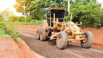Image of a grader machine leveling gravels on a dirt road in preparation for asphalt paving for new road construction. photo