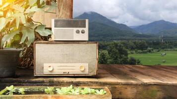 Image of almost rotten gray old fashion radio receivers on wooden planks floor with blur field and mountains view background. photo