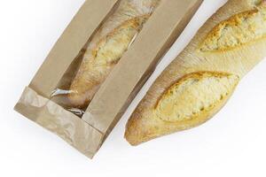 Two freshly baked baguettes, one wrapped in brown paper bag, Artisan French baguettes with crispy crusts in paper packaging. Isolated on a white background. Closeup. With clipping path photo