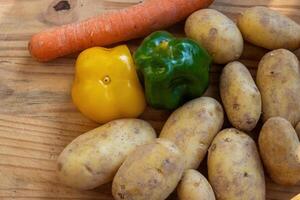 Potatoes, green, yellow bell peppers, carrot on a rustic wooden cutting board for healthy cooking and meal preparation. A vibrant assortment of fresh vegetables farm-to-table concept. Top view photo