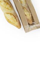 Two freshly baked baguettes, one wrapped in brown paper bag, Artisan French baguettes with crispy crusts in paper packaging. Isolated on a white background. Closeup. With clipping path photo