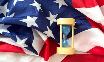 Hourglass on table with USA flag in the background. Sand glass on old wooden table with American flag in the background, vertical image. photo