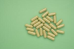 Flat lay of Andrographis paniculata capsules isolated on a green background. Space for text. Herbal, medicine, and healthcare concept photo