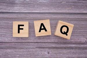 The FAQ word is written on wooden cubes on wooden table background. Frequently asked questions. Top view. Close-up photo