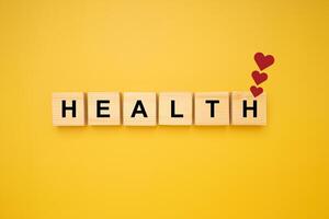 HEALTH word is written on wood blocks with three red heart symbols isolated on a yellow background. Top view. Close-up photo. Health and healthcare concept photo