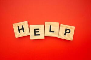 HELP word is written on wood blocks isolated on a red background. Top view. Close-up photo