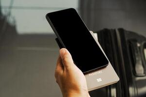Hand holding of a smartphone with suitcase background. Close-up photo. Space for text. Technology and communication concept photo