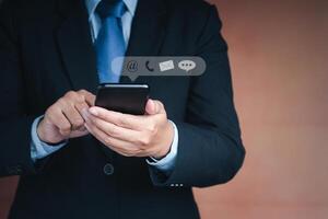 Hands of a businessman using a smartphone with the icon images while standing with a brown background. Close-up photo. Communication, technology, and business customer support concept photo