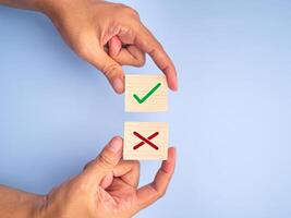 Hand of holding green checkmark and red cross symbol on wooden blocks on light blue background. Top view. Flat lay. Space for text photo