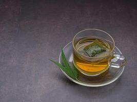 A cup of hemp tea and marijuana leaf laid on vintage background. Cannabis herbal tea. Close-up photo. Selective focus. Relaxation concept photo