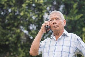 A senior man is using a smartphone looking up and a worried face while standing outdoors in the garden. Space for text. Aged people and communication concept photo