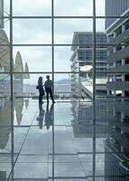 Airport terminal huge glass window with view of departure buildings and silhouette of two persons photo