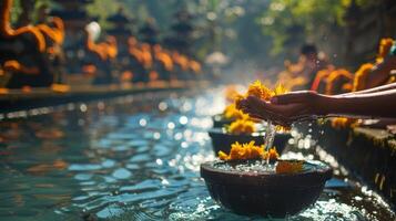 Hands holding yellow flowers pouring water into a stone bowl during a spiritual cleansing ritual at a temple in bali photo