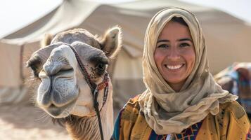 Tour guide woman in traditional attire poses with a camel and smiles in the desert photo
