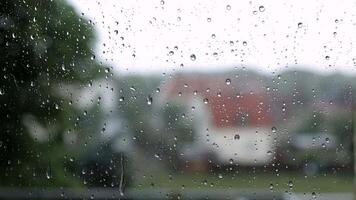 City view through a window on a rainy day. Rain drops on window with clouds, light bokeh background. Focus on drops on glass. Blurred tree and houses, feeling cool, free space for texts. video