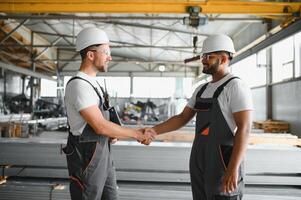 Two engineers in hard hats shake hands in a factory. photo