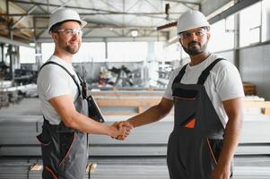 Two engineers in hard hats shake hands in a factory. photo
