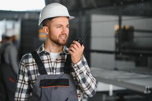 Smiling and happy employee. Portrait of industrial worker indoors in factory. Young technician with white hard hat photo