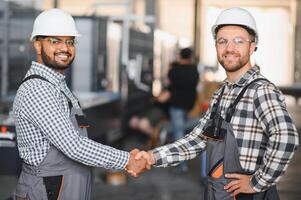 Two engineers in hard hats shake hands in a factory. photo