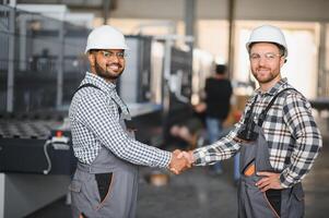 Two engineers in hard hats shake hands in a factory. photo