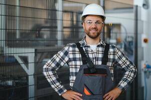 Smiling and happy employee. Portrait of industrial worker indoors in factory. Young technician with white hard hat photo
