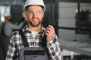 Smiling and happy employee. Portrait of industrial worker indoors in factory. Young technician with white hard hat photo