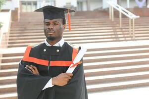 I have finally graduated. Happy young African man in graduation gowns holding diploma photo