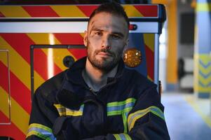 Portrait of a firefighter in a protective suit and a protective helmet standing by a fire engine after working on a fire. Close-up image photo