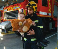A firefighter take a little child boy to save him. Fire engine car on background photo