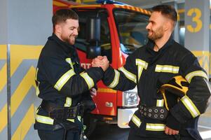 Portrait of two young firemen in uniform standing inside the fire station photo