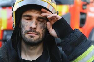 Portrait of a firefighter in a protective suit and a protective helmet standing by a fire engine after working on a fire. Close-up image photo