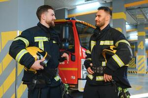 Portrait of two young firemen in uniform standing inside the fire station photo