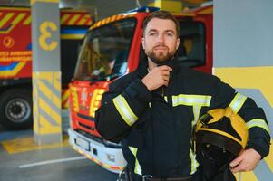fireman in protective uniform standing near fire engine on station photo
