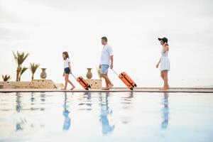 young family with suitcases walking to hotel building with beautiful swimming pool. traveling and relaxing time concept. photo