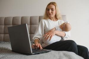 young woman with a small child works from home. Working remotely during a lockdown. freelancer or remotely employed specialist is sitting on a bed with a laptop and trying to concentrate photo