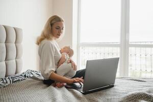 young woman with a small child works from home. Working remotely during a lockdown. freelancer or remotely employed specialist is sitting on a bed with a laptop and trying to concentrate photo