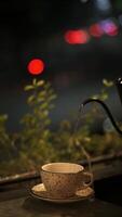 Gießen heiß Wasser in ein Tasse auf draussen Tabelle im beim Nacht mit bunt Bokeh Hintergrund video