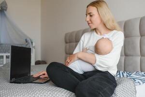 young woman with a small child works from home. Working remotely during a lockdown. freelancer or remotely employed specialist is sitting on a bed with a laptop and trying to concentrate photo