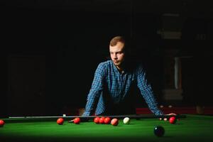 Young man playing billiards in the dark billiard club photo