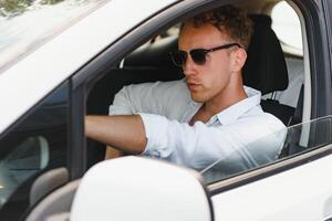 Test driving of new generation electro vehicle with self driving system. Handsome Caucasian man sitting behind the wheel of new modern car and smiling at camera. photo