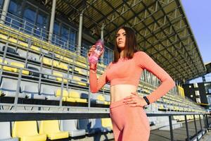 hermosa joven deportivo mujer Bebiendo agua después correr. ajuste persona que practica jogging niña tomando un descanso después deporte. estilo de vida, gente, deporte y ocio concepto. foto