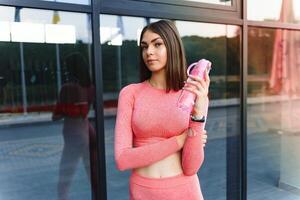 hermosa joven deportivo mujer Bebiendo agua después correr. ajuste persona que practica jogging niña tomando un descanso después deporte. estilo de vida, gente, deporte y ocio concepto. foto