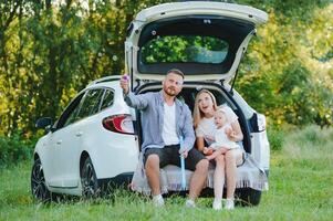 Young family three people in white clothes have picnic. Beautiful parents and daughter travel by car during summer vacation. Scene in park photo