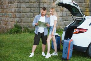 Young couple standing near the opened car boot with suitcases. photo
