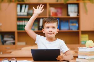 Elementary schoolboy using digital tablet with classmate studying in background at classroom photo